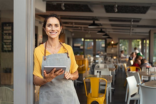 Portrait-of-happy-woman-standing-at-doorway-of-her-store.-Cheerful-mature-waitress-waiting-for-clients-at-coffee-shop.